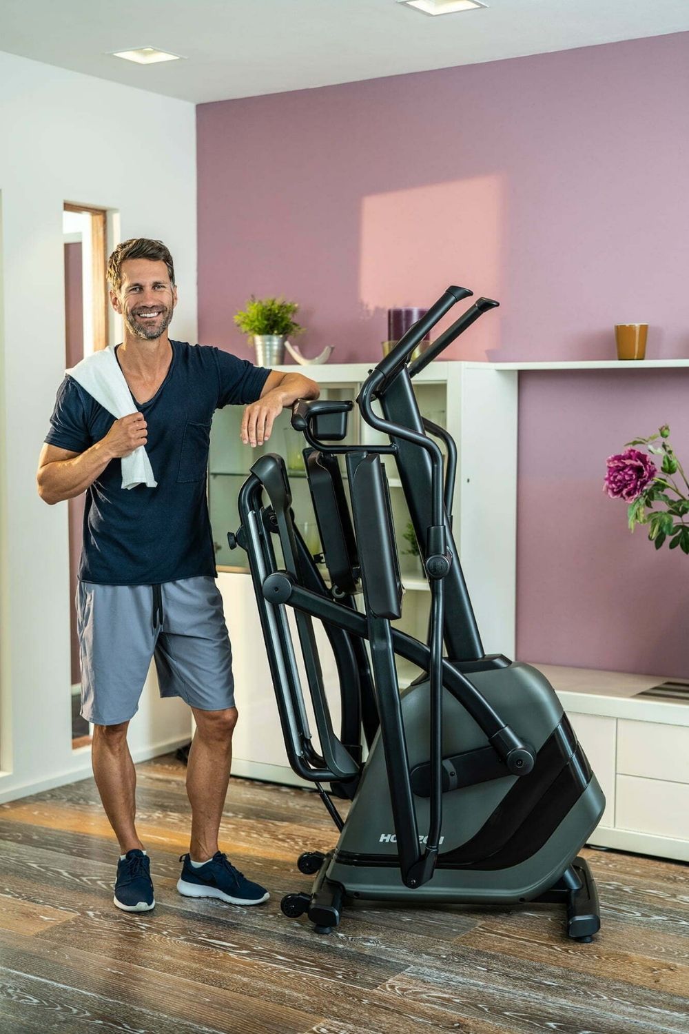 Muž v byte stojaci vedľa zloženého eliptického trenažéra